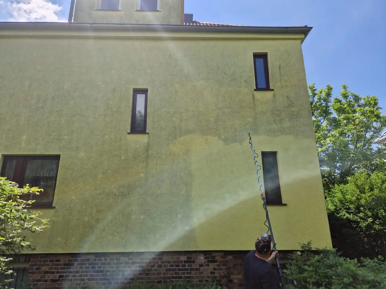 Mitarbeiter reinigt eine Hausfassade schonend mit der Teleskoplanze